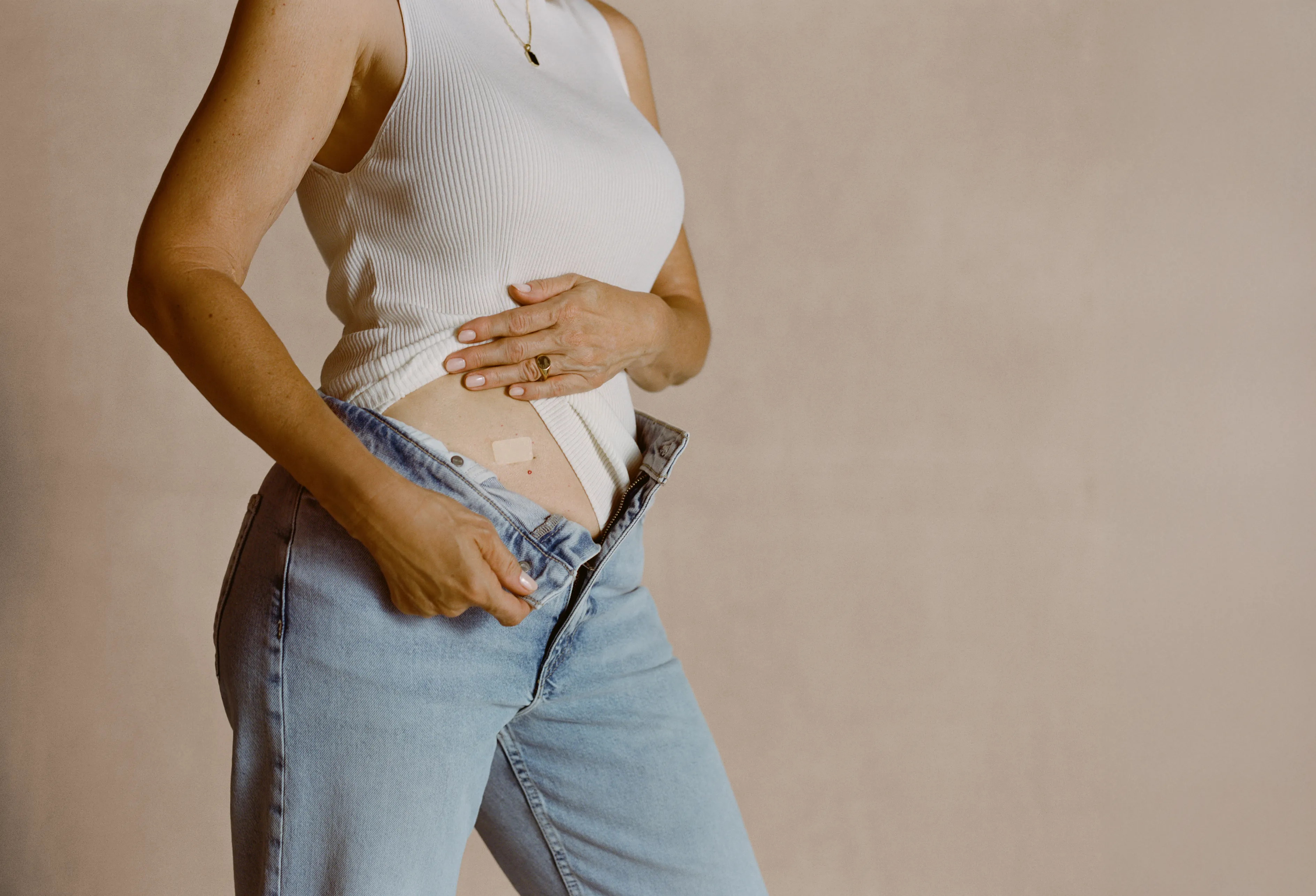 Close-up of a woman applying an HRT patch on her lower abdomen as part of menopause hormone therapy. Close-up of a woman applying an HRT patch on her lower abdomen as part of menopause hormone therapy.